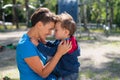 The woman gently hugs her son on the playground. The little boy is naughty and his mother calms him down