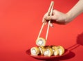 Women hand hold sushi rolls with chopsticks. Red background with hard shadow. Creative concept. Royalty Free Stock Photo