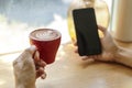 Women hand holding cofffee latte, cappuccino cup in cafe with blur hand show smart, mobile phone. Hand hold red cup coffee relax Royalty Free Stock Photo