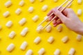 Women hand holding corn sticks on wooden chopsticks. Sweet corn sticks on yellow background