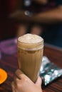 Women hand is holding a glass of Teh tarik or pulled tea is a famous sweet milk tea in Malaysia.