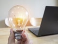 Women hand holding light bulb with laptop on wooden desk Royalty Free Stock Photo