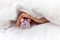 Women Hand holding pink alarm clock in bed. Concept of world sleep day.