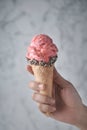 Women hand holding strawberry ice cream and waffle cone decorated with white sesame and black sesame on marble background Royalty Free Stock Photo