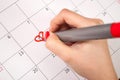 Women hand with pencil drawing heart shape in calendar for Valentines day