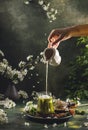 Women hand is pouring homemade sour cream from small jar to glass with matcha tea