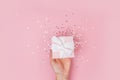 Women hands holding a gift or gift box decorated with confetti on a pink pastel table top view Royalty Free Stock Photo