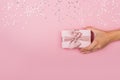 Women hands holding a gift or gift box decorated with confetti on a pink pastel table top view Royalty Free Stock Photo