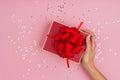 Women hands holding a gift or gift box decorated with confetti on a pink pastel table top view Royalty Free Stock Photo