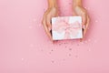 Women hands holding a gift or gift box decorated with confetti on a pink pastel table top view Royalty Free Stock Photo