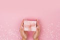 Women hands holding a gift or gift box decorated with confetti on a pink pastel table top view Royalty Free Stock Photo