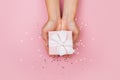 Women hands holding a gift or gift box decorated with confetti on a pink pastel table top view Royalty Free Stock Photo