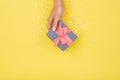 Women hands holding a gift or gift box decorated with confetti on a yellow background top view Royalty Free Stock Photo