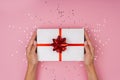 Women hands holding a gift or gift box decorated with confetti on a pink pastel table top view Royalty Free Stock Photo