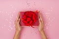 Women hands holding a gift or gift box decorated with confetti on a pink pastel table top view Royalty Free Stock Photo