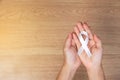 women hands holding white bow, white ribbons on wooden background. Awareness White ribbon for campaign to end violence against