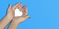 Women hands holding a white heart in blue background top view. Kindness, charity and compassion concept