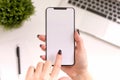 Women hands holding the white phone with isolated screen above the table with computer Royalty Free Stock Photo