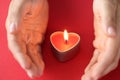 Women hands protect burning fire in candle in form of heart closeup