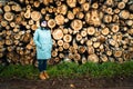 Women in her thirties with blue rain coat poses in front of birch tree log stack - forest scenery with wood ready to be produced