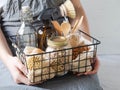 Women hold a black metal basket with eco-friendly kitchen set. Food, brushes, wood appliances, bags, bottle and jar