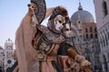 Women masks holding fans and wearing ornate gold and black costume standing in front of the Doges Palace during Venice Carnival