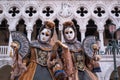 Women masks holding fans and wearing ornate gold and black costume standing in front of the Doges Palace during Venice Carnival