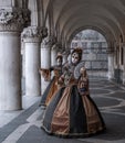 Women masks holding fans and wearing ornate gold and black costume under arches at the Doges Palace during Venice Carnival