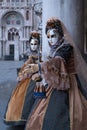 Women masks holding fan and wearing ornate gold and black costume under the arches at the Doges Palace during Venice Carnival