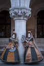 Women masks holding fans and wearing ornate gold and black costume under the arches at the Doges Palace during Venice Carnival