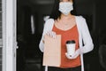 Woman holding takeaway food in paper bag and a cup of coffee from delivery service during coronavirus pandemic situation at home Royalty Free Stock Photo