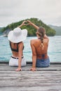 Women, lake and friends outdoor with heart hand sign on deck to relax with peace, water and love. Back of female people Royalty Free Stock Photo