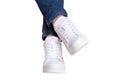 Women legs in jeans and sneakers. Woman legs in blue denim pants wearing modern white sneaker. Fashionable white footwear. Macro