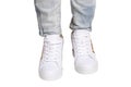 Women legs in jeans and sneakers. Woman legs in light denim pants wearing modern white sneaker. Fashionable white footwear. Macro Royalty Free Stock Photo