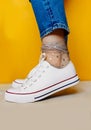 Women legs in white clean new sneakers, transparent thin socks with silver shiny stars and blue jeans on yellow background.