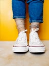 Women legs in white clean new sneakers, transparent thin socks with silver shiny stars and blue jeans on yellow background.