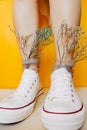 Women legs in white clean new sneakers, transparent thin socks with silver shiny stars and and dry flowers in them on yellow