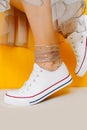Women legs in white clean new sneakers, transparent thin socks with silver shiny stars and lush tulle dress on yellow background.
