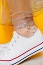 Women legs in white clean new sneakers, transparent thin socks with silver shiny stars and lush tulle dress on yellow background.