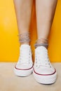 Women legs in white clean new sneakers, transparent thin socks with silver shiny stars on yellow background. combination of sports