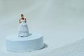 Women miniature people stand above white podium trying wedding dress.