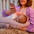 A woman mother breastfeeding an infant baby with a phone in her hands for online consultations Royalty Free Stock Photo