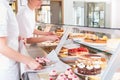 Women in pastry shop filling up sales display with pies