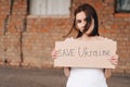 Women with Poster Save Ukraine. A woman with a belligerent look looks into the Camera