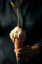 Women pouring caramel on a cone of caramel ice cream. Dark grey background.