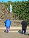 Women prayers in front of a Lourdes grotto, catholic shrine.