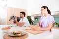 A woman is preparing breakfast. A man sits next to a table and collects a robot.