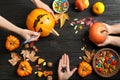 Women preparing Halloween pumpkin head jack lantern and holiday decorations on wooden table, flat lay composition Royalty Free Stock Photo