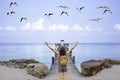 Women raise their arms and shoulder backpack on wooden bridge pier boat in the sea and the birds flying in the sky at Koh Kood, Royalty Free Stock Photo