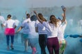 Women run in a holi color run race with arms raised with blue powder swirling around them - unrecognizable people